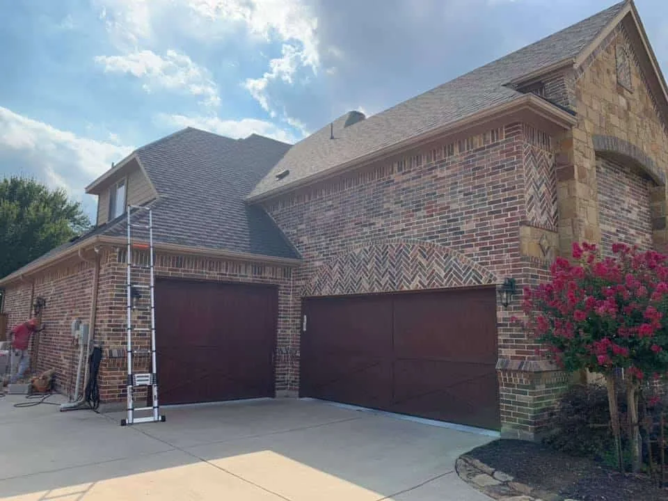 Two-story brick home with a finished dark roof and ladder on site